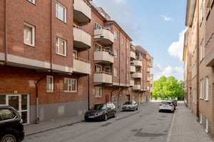 Flerfamiljshus i tegelfasad med takkupor och vita balkonger, längs med gata med parkerade bilar