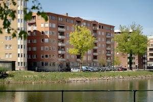 Flerfamiljshus i tegel och ljusa balkonger, omgiven av grönska och gata med vattenkanal i förgrunden