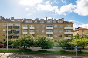 Flerbostadshus i gul tegelfasad med vita balkonger och vindskupor, omgivet av gata med parkerade bilar och träd