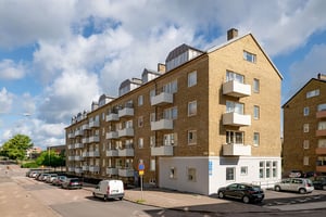 Flerbostadshus i gul tegelfasad med vita balkonger och vindskupor, omgivet av gata med parkerade bilar