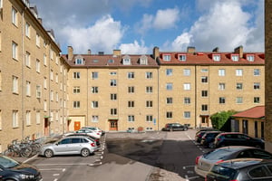 Flerbostadshus i gul tegelfasad med vindskupor, med parkering på innergården