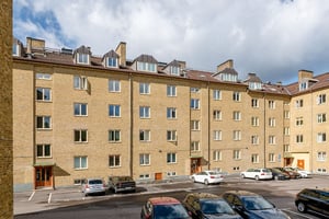 Flerbostadshus i gul tegelfasad med vindskupor, med parkering på innergården