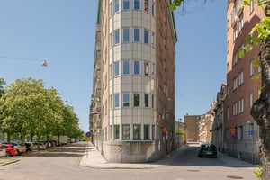 Gavel på flerbostadshus i tegelfasad med ljusa detaljer, i vinkel längs gator med parkerade bilar och blommande kastanjeträd