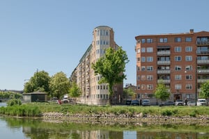 Flerbostadshus med tegelfasad och ljusa detaljer i vinkel, längs med gata och vattenkanal i förgrunden