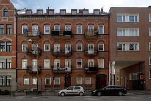 Flerbostadshus i rött tegel och grå puts med detaljer kring fönster vinskupor, längs gata med parkerade bilar