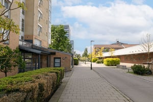 Flerfamiljshus i ljus fasad längs stenbelagd trottoar och cykelbana