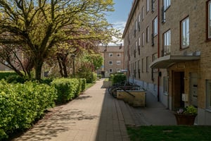 Flerfamiljshus i tegel med franska balkonger, med stenbelagd gång mellan huset och en grön innergård