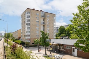 Flerfamiljshus i ljus fasad med inglasade balkonger, med en lägre byggnad som innefattar pizzeria i förgrunden