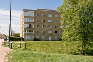 Flerfamiljshus i gult tegel med burspråk och inglasade balkonger, omgivet av grönska
