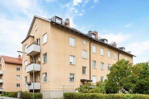 Flerbostadshus i ljus puts längs lokalgata, med träd och buskar kring området
