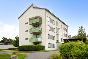 Flerbostadshus i ljus puts, med gröna balkonger och grönska på innergård