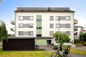 Flerbostadshus i ljus puts, med mörkt gårdshus framför huset samt parkerad cykel