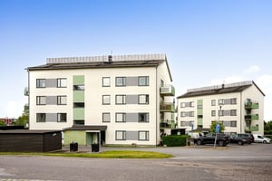 Flerbostadshus i ljus puts, med gröna balkonger och parkeringsplats