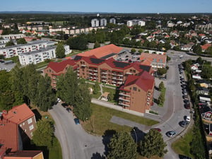 Flygvy över bostadshus i ett bostadsområde med röda tak, parkering och grönska