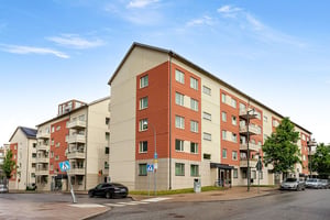 Flerbostadshus i puts och tegel längs lokalgata med parkerad mörk bil