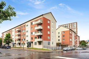 Flerbostadshus i puts och tegel längs lokalgata med parkerade bilar