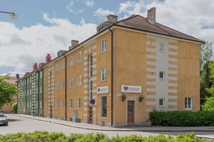 Flerbostadshus i gult och grönt med innergård, balkonger och skyltar vid gatan