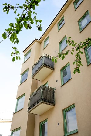 Hyresrättsfastighet i gul nyans med gröna detaljer kring fönster och balkonger
