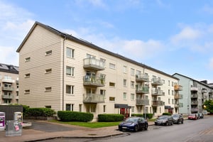 Hyresrättsfastighet med balkonger ut mot lokalgata, med parkerade bilar
