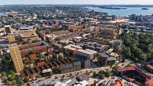 Flygvy över en stad med flera bostadshus, vägar och vatten i bakgrunden