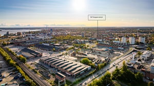 Flygvy över stadsdel med byggarbetsplats märkt Brf Kopparvalvet, järnvägsspår, vägar och stadsmiljö i kvällsljus
