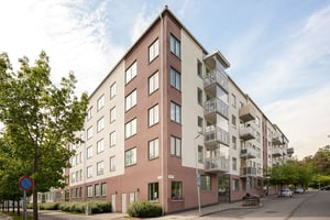 Hyresrättsfastighet med balkonger, med träd framför huset längs lokalgata