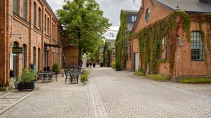 Kullerstensgata mellan röda tegelbyggnader med uteservering och grönskande fasader
