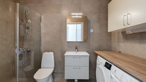 Modernt tvättutrymme med dusch, toalett, handfat och tvättmaskin. Beige kakel och förvaringsskåp