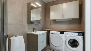 Tvättstuga med tvättmaskin, torktumlare, handfat och förvaringsskåp i modern inredning