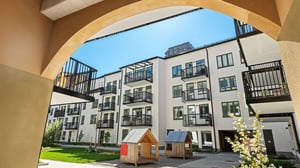 Moderna bostadshus med balkonger och innergård, sedd genom en bågöppning