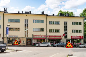 Bostadshus med flera butiker och restauranger i bottenvåningen, med parkerade bilar och vägarbetsskyltar framför