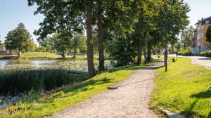 Promenadstig längs en sjö i Strängnäs med träd, gräs och bostadshus i bakgrunden