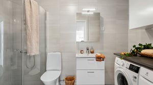 Inflyttningsklart badrum med dusch, tvättställ, spegelskåp och tvättmaskin. Modern bostad med ljusa kakelväggar