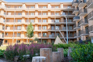 Flerfamiljshus med balkonger och grön innergård med blommor och träpallar