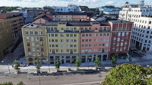 Flerfärgad fasad på en rad moderna byggnader längs en gata, med träd och parkeringsplatser i förgrunden