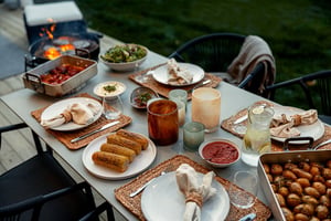 Uppdukad matplats utomhus med grillad mat, sallader, majs, potatis och drycker på ett bord