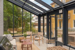 Inglasad uteplats med soffgrupp, två trästolar och bord i en bostadsmiljö