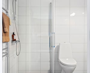 Inflyttningsklart badrum med dusch, vita kaklade väggar och toalett