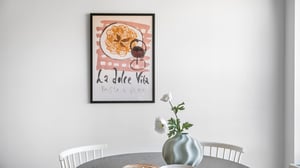 Ljust matrum med rund bord, vita stolar, vas med vita blommor och tavla på väggen