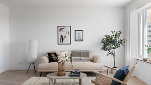 Inflyttningsklart vardagsrum med beige soffa, soffbord, golvlampa, växt och ljusa väggar