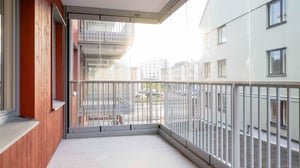 Inglasad balkong med utsikt över ett bostadsområde, med glasräcken och trägolv på ena sidan