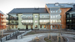 Flerfamiljshus med moderna fasader, stora glaspartier och balkonger, omgivna av en nyanlagd gård med stensatta gångvägar och planteringar