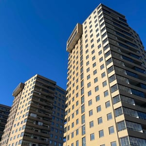 Flerbostadshus med ljus fasad och mörka balkongpartier mot blå himmel