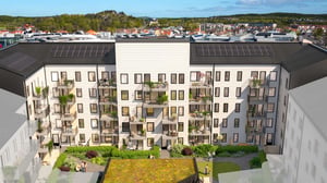 Illustration av flerbostadshus med balkonger, solpaneler och grön innergård