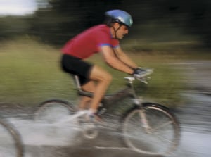 Person cyklar på en stig genom vatten, med hjälm och röd cykeltröja