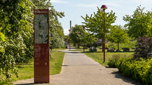 Promenadstig i en grön park i Helsingborg med informationsskylt och rödbruna lampstolpar