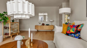 Vardagsrum med ljus inredning, beige soffa med färgglada kuddar, träbord och stora taklampor