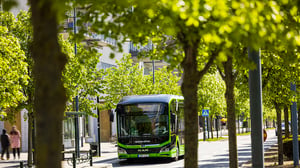 Grön Skånetrafiken-buss kör på en trädkantad stadsgata med bostadshus i bakgrunden i Malmö