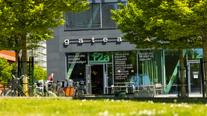 Bageri och café med uteservering i stadsmiljö, omgivet av gröna träd och cyklar