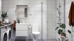 Modernt badrum med tvättmaskin, dusch, toalett och kommod i vitt kakel